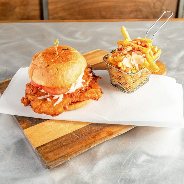 Crispy chicken sandwich with tomato and shredded lettuce, served with a basket of parmesan fries.