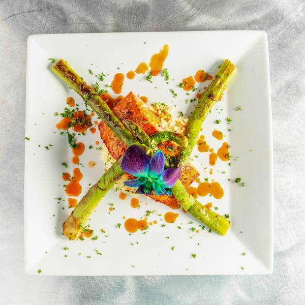 Salmon with asparagus, rice, orange sauce, parsley, and a purple orchid on a white plate.