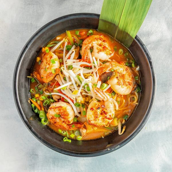 Shrimp ramen with bean sprouts, green onions, and vegetables in a black bowl.