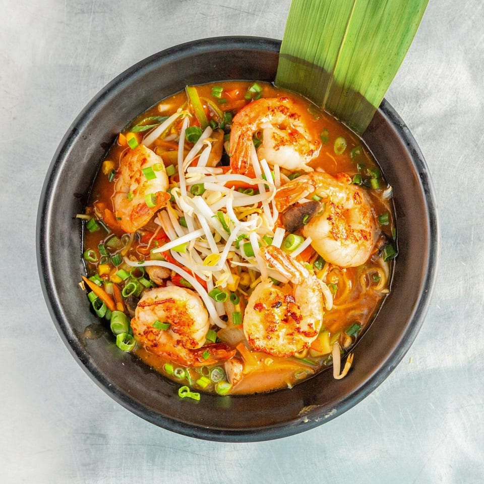 Shrimp ramen with bean sprouts, green onions, and vegetables in a black bowl.