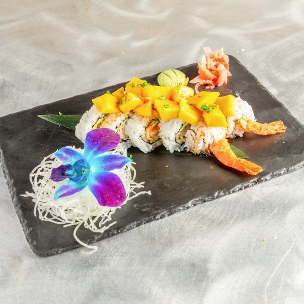 Sushi roll with mango, shrimp, wasabi, and pickled ginger, garnished with an orchid.