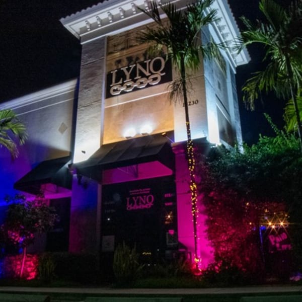 The LYNQ restaurant exterior at night, illuminated with vibrant blue and pink lights.