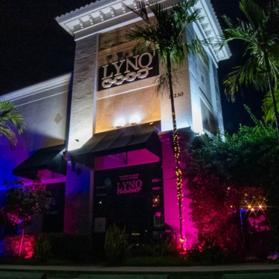 The LYNQ restaurant exterior at night, illuminated with vibrant blue and pink lights.