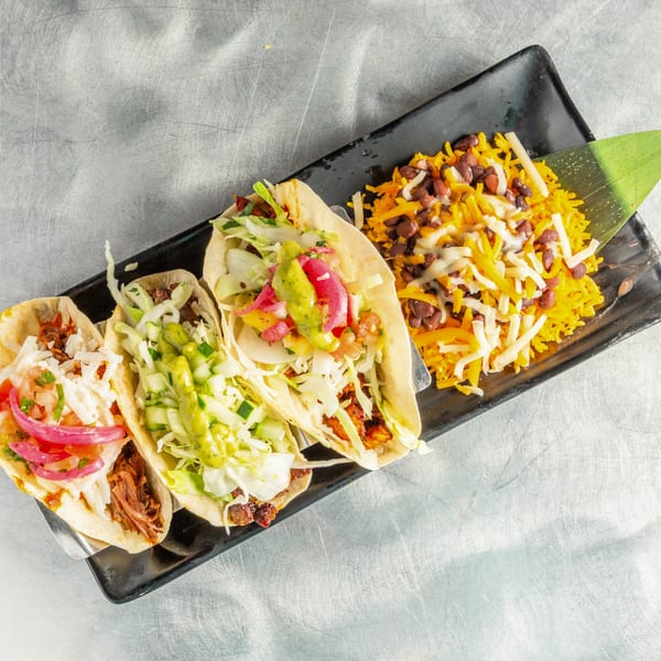 Three tacos with various fillings and toppings, served with yellow rice, beans, and cheese.