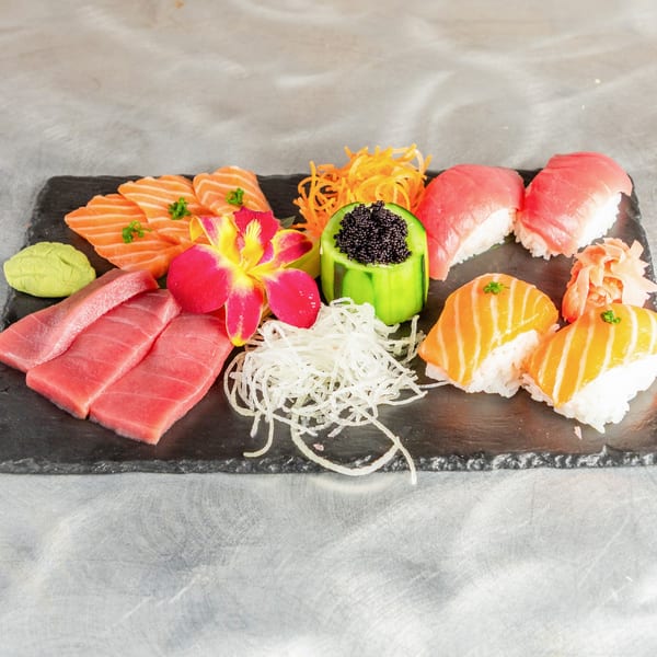 Assorted sushi and sashimi platter with tuna, salmon, wasabi, ginger, and a decorative orchid.
