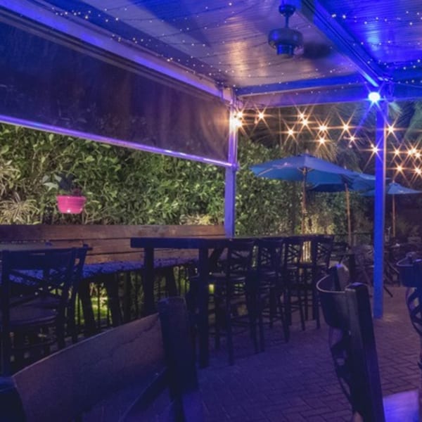 LYNQ's outdoor patio at night with blue lighting, string lights, tables, chairs, and umbrellas.