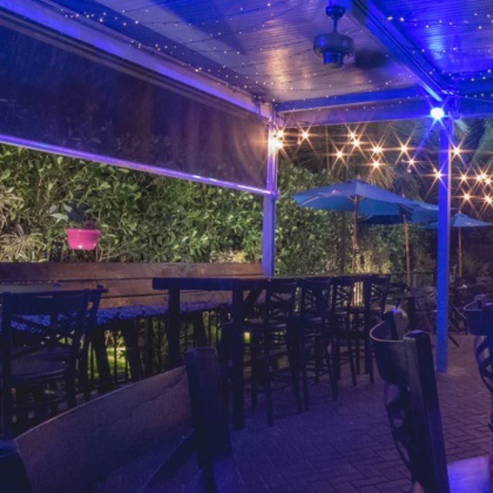 LYNQ's outdoor patio at night with blue lighting, string lights, tables, chairs, and umbrellas.