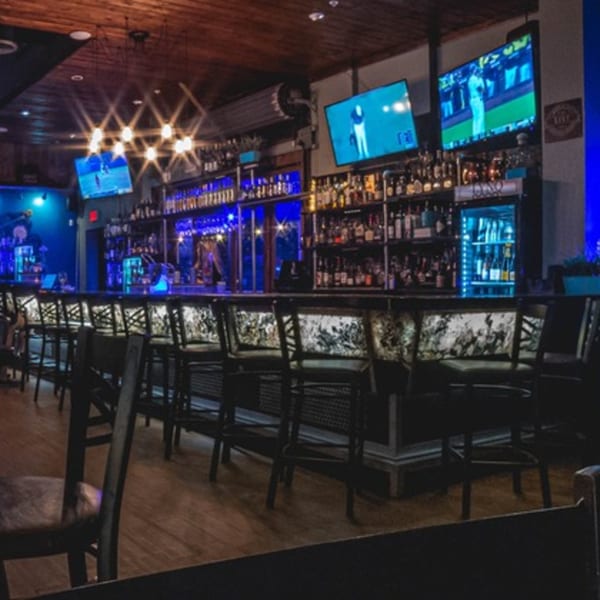LYNQ's bar area with blue lighting, bar stools, and multiple TVs showing sports.